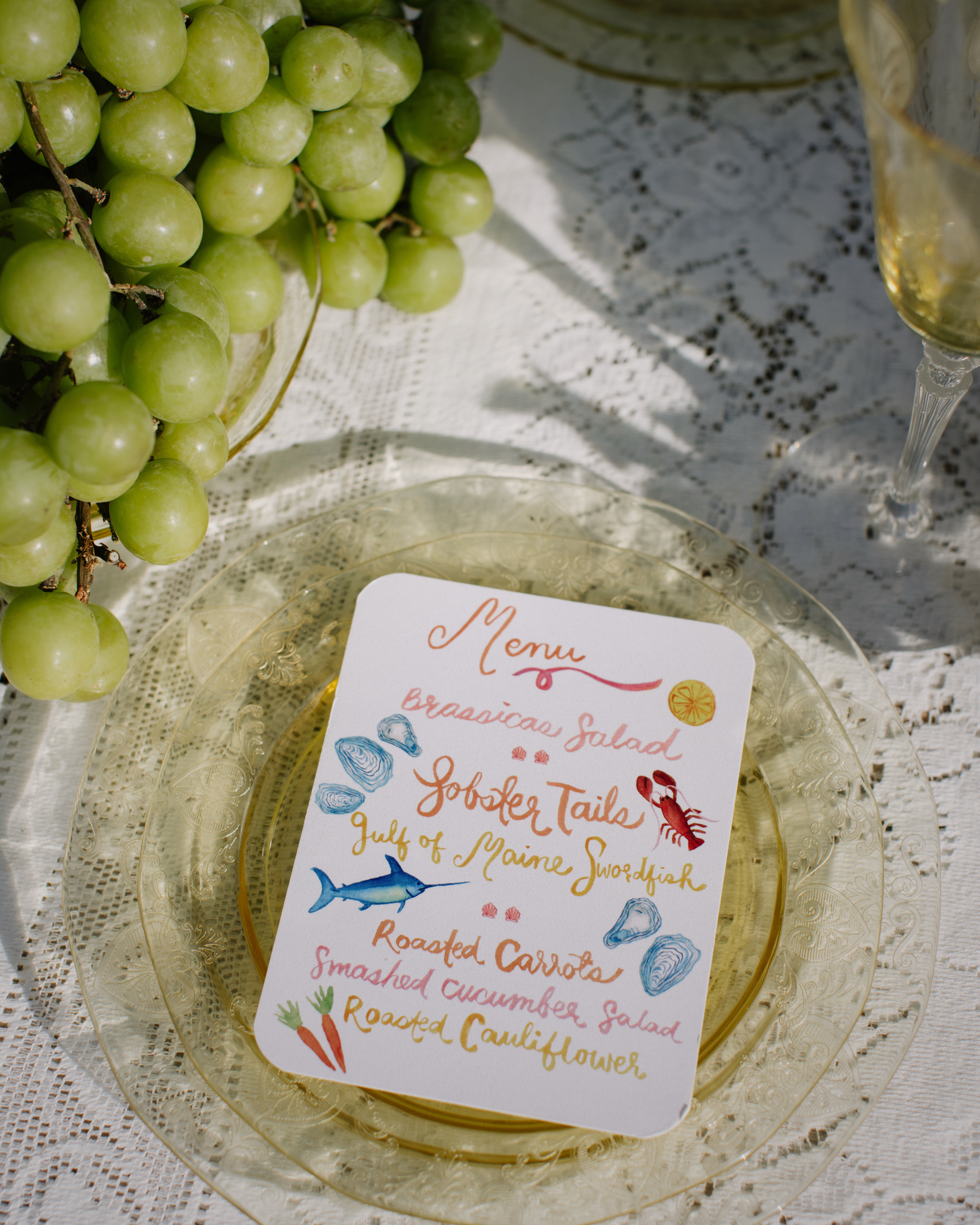 Menu card on a glass plate with grapes and a glass of white wine in the background