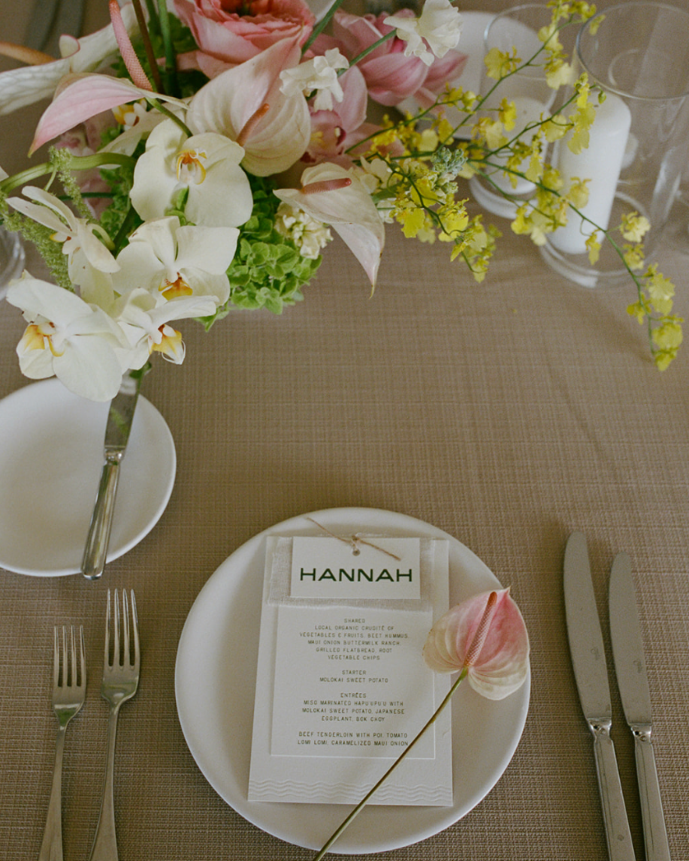 Table setting with floral arrangement, name card, and cutlery on a textured tablecloth.
