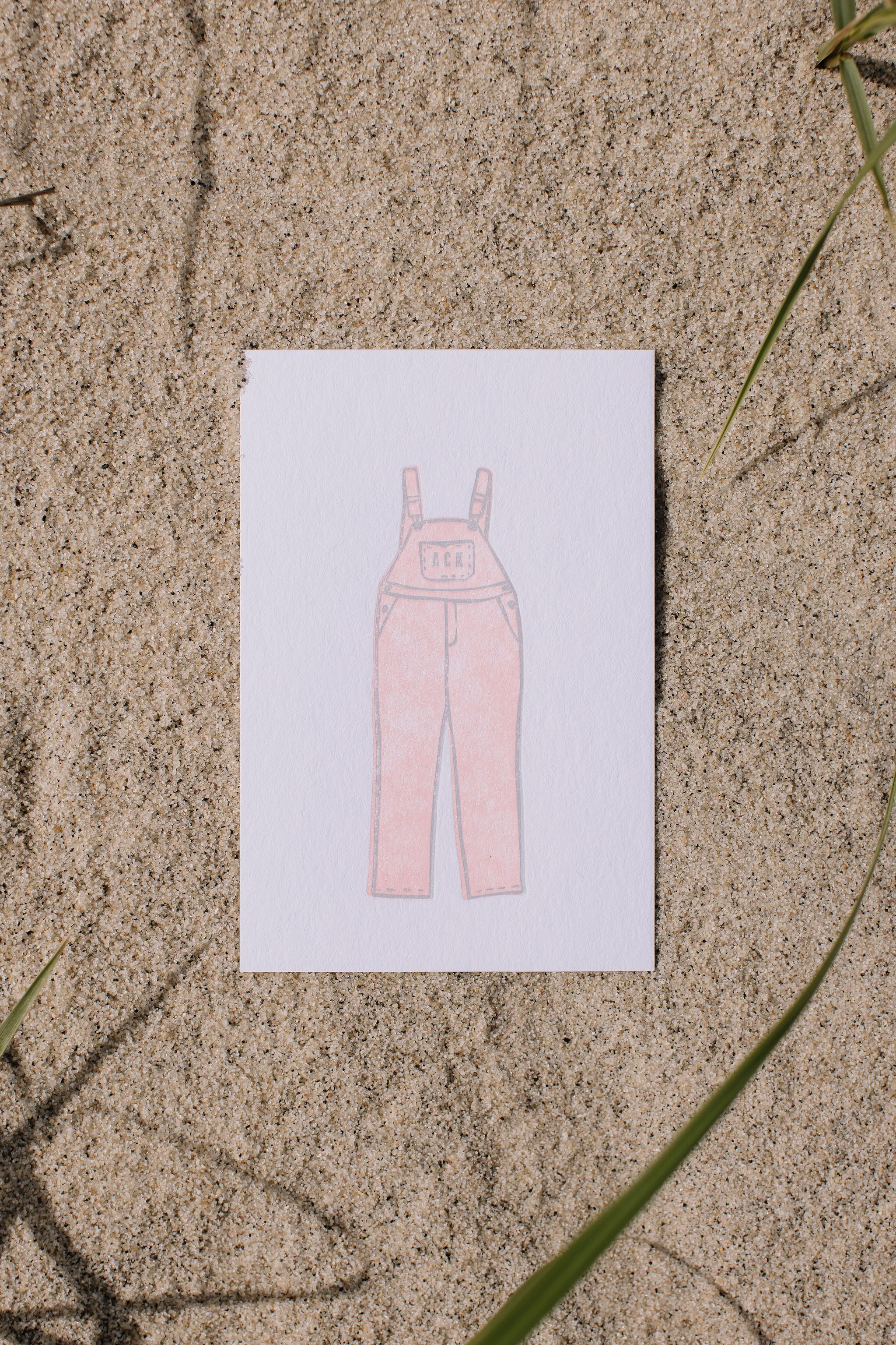 ACK postcard with a pink overalls illustration on a sandy surface
