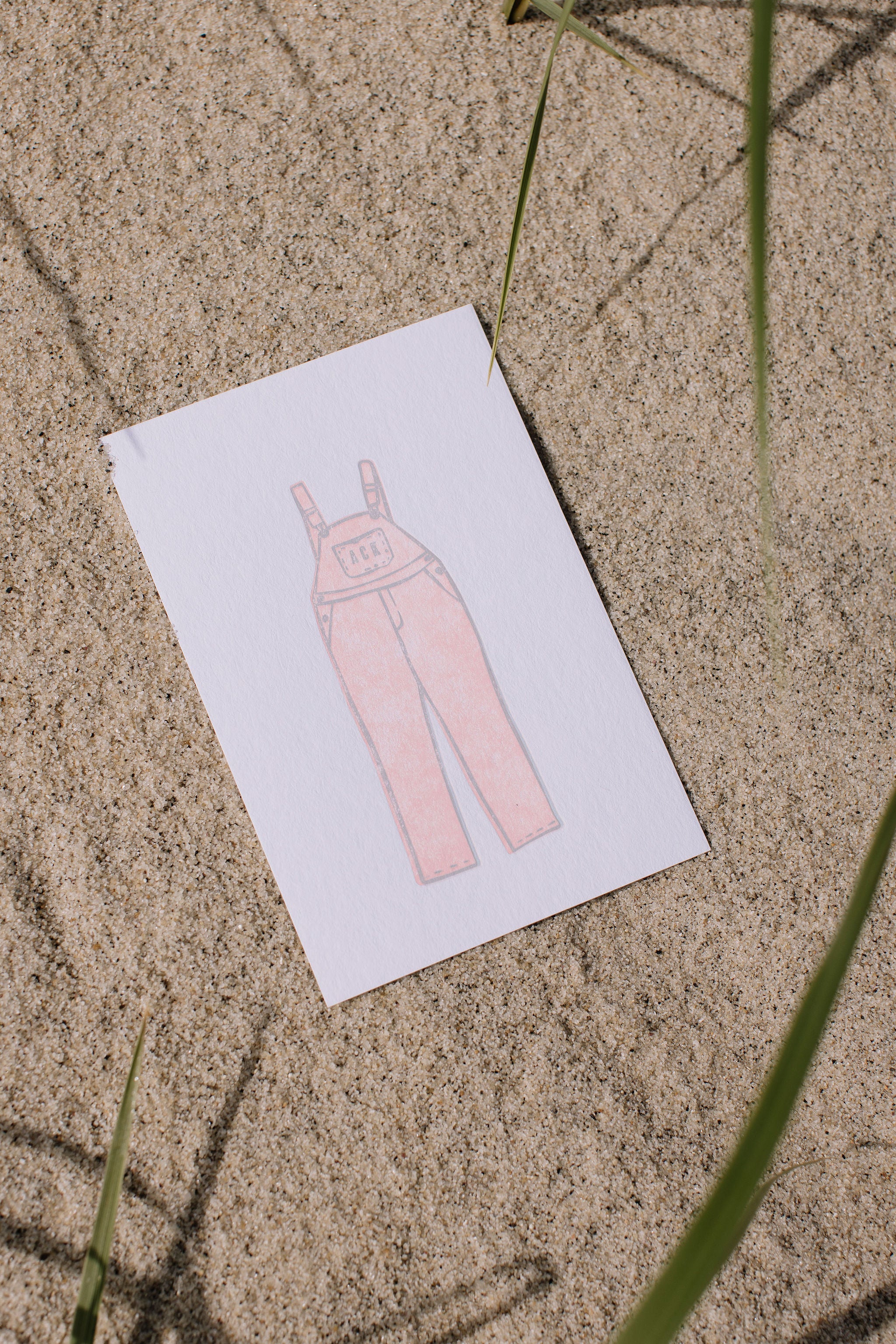 ACK postcard with a pink overalls illustration on a sandy surface