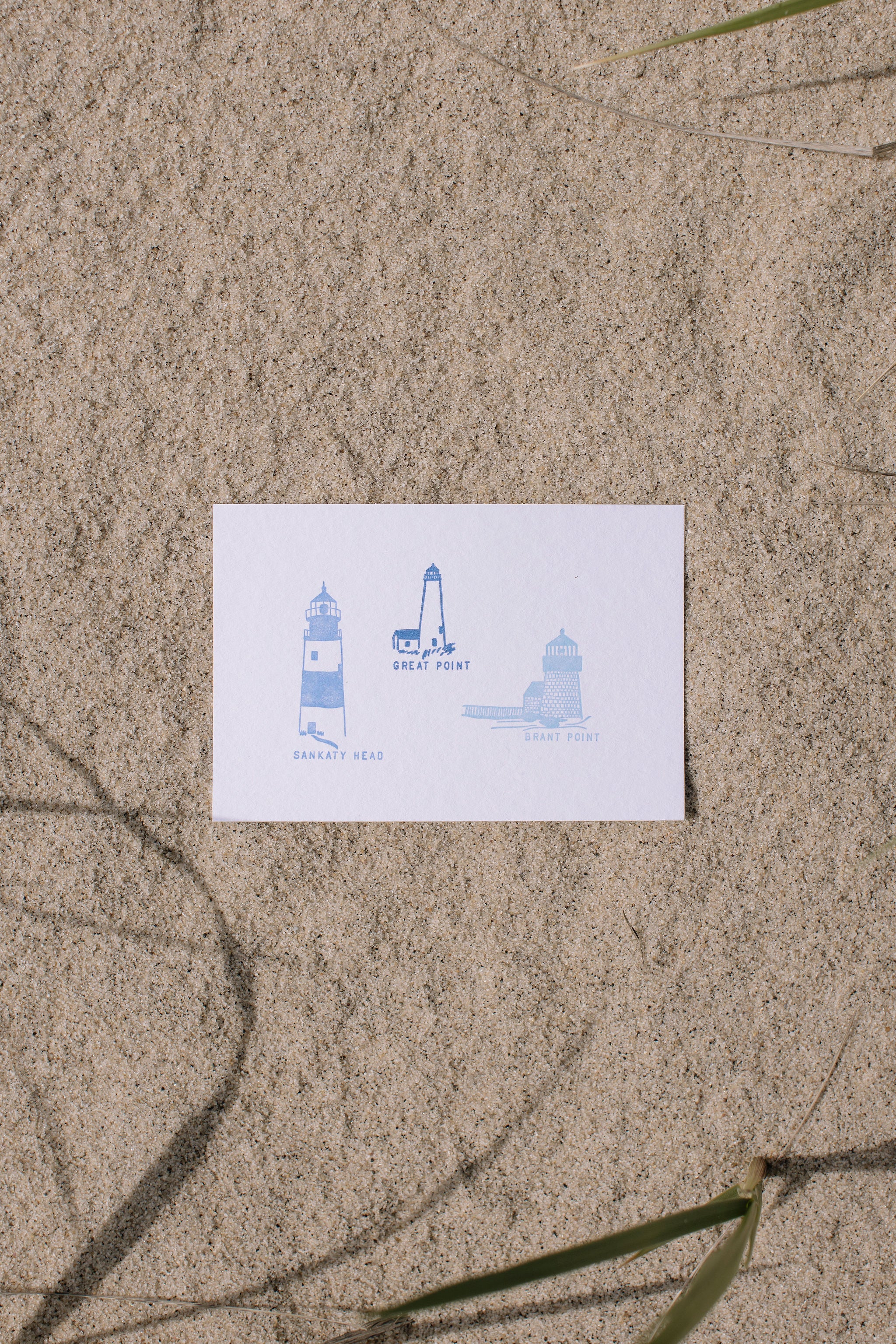 Postcard with blue lighthouse illustrations on sand