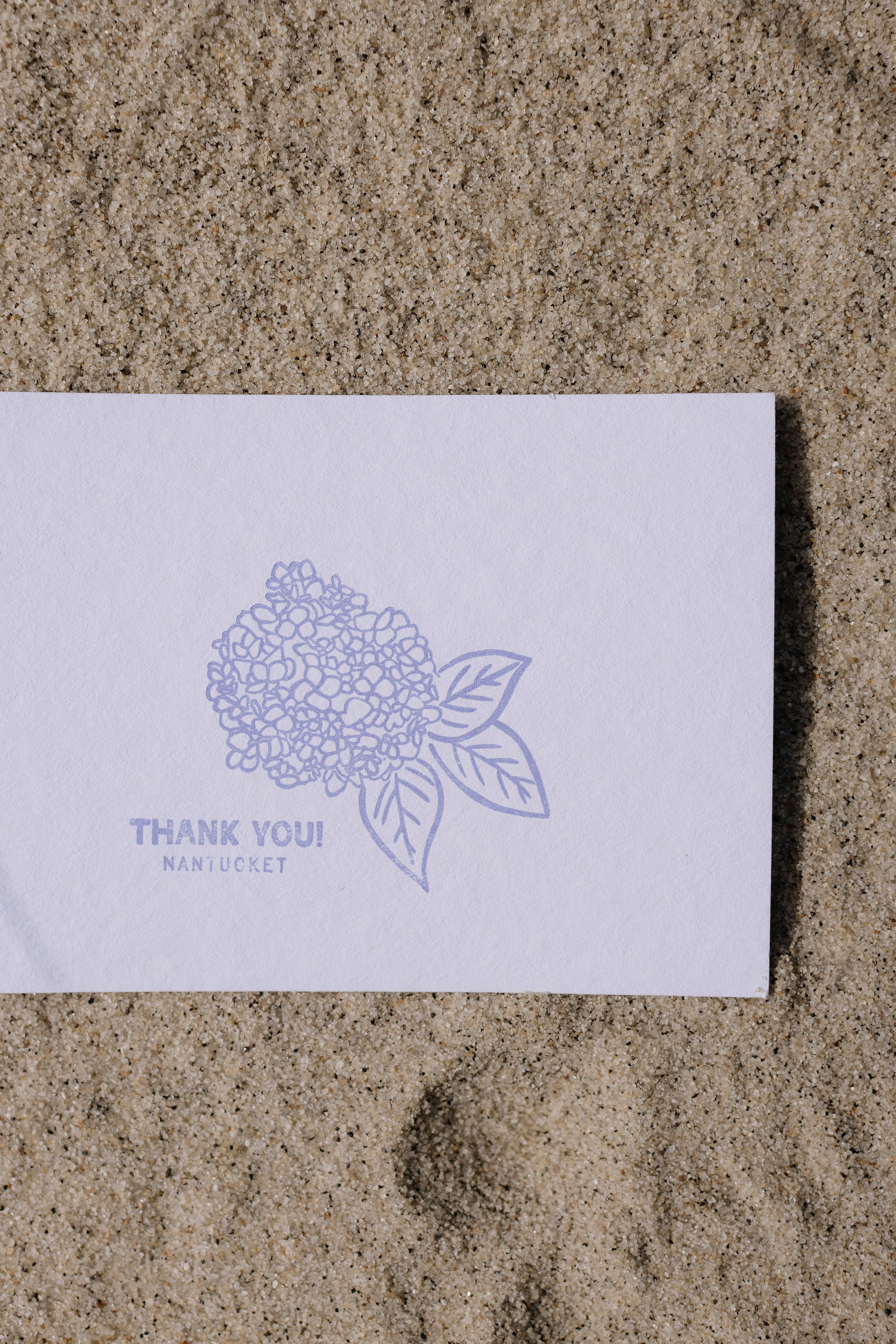 White thank you postcard with blue floral design and text on sandy ground