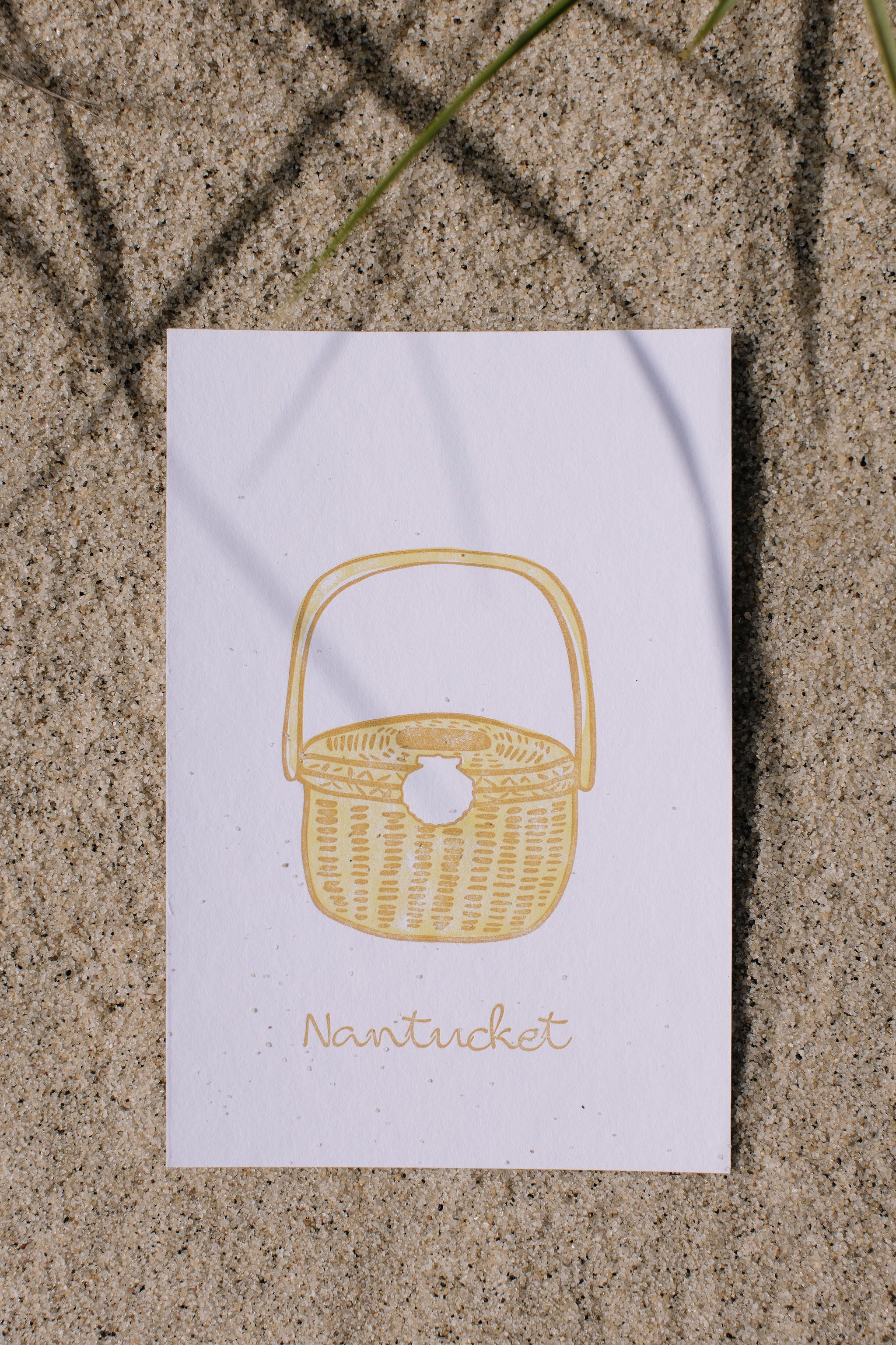 White postcard with a yellow wicker basket illustration on sand