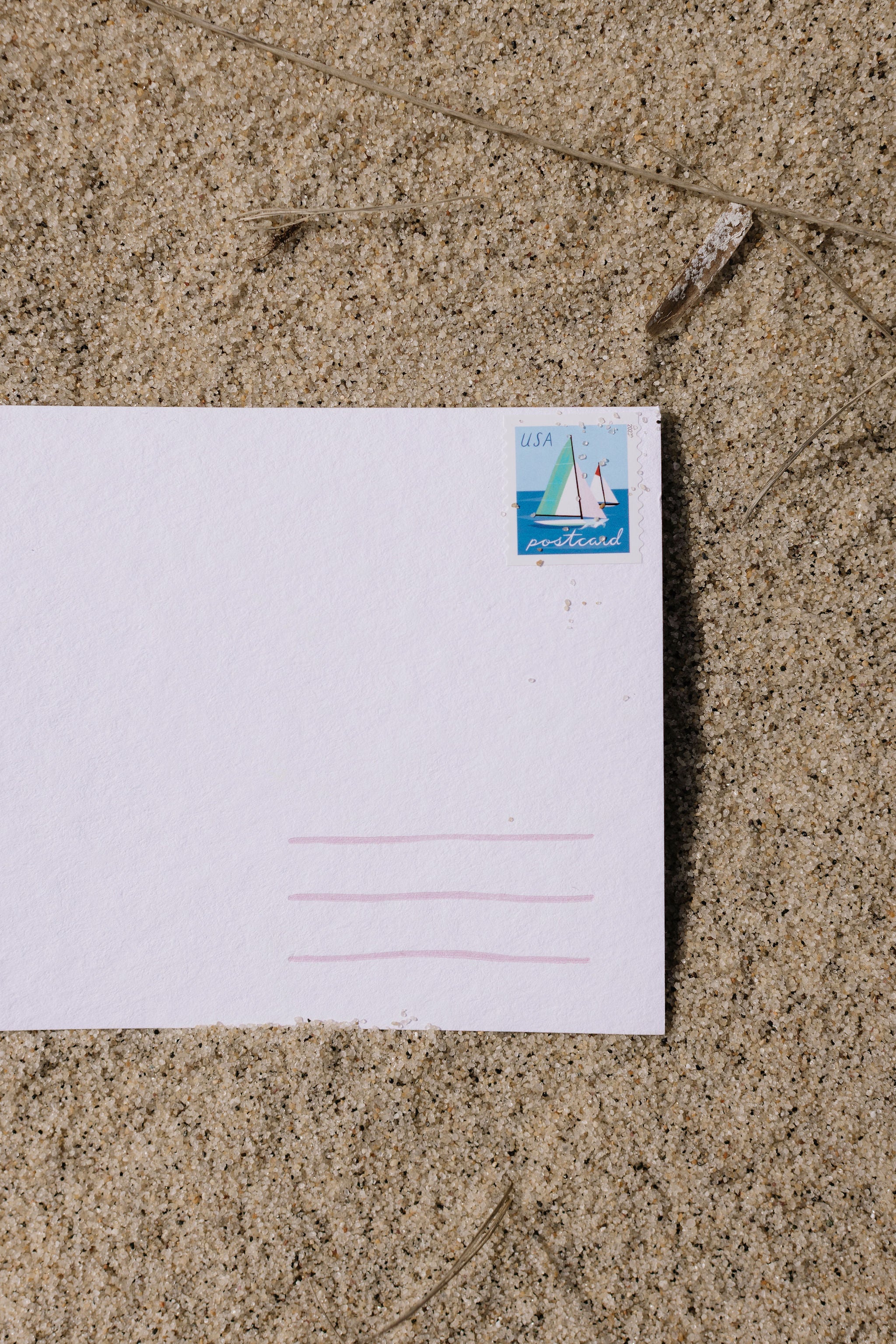 White envelope with a sailboat stamp on sand